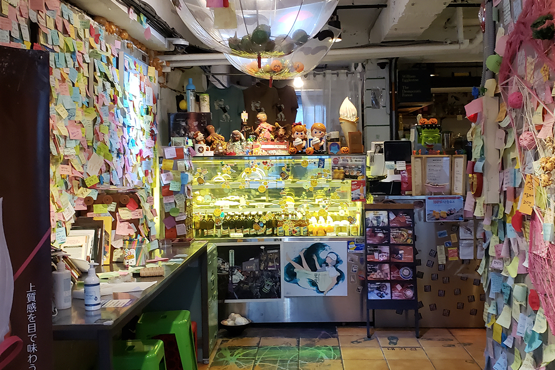 文畫裝咖啡廳內部，牆上掛滿了彩色貼紙和裝飾。