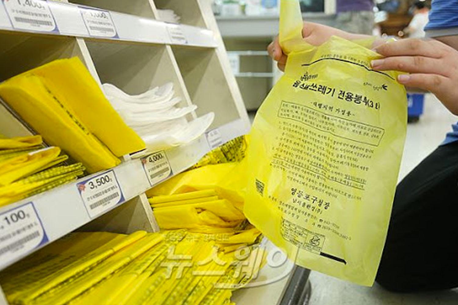 마트의 진열대에 배열된 다양한 쓰레기 봉투 및 구매하고 있는 고객의 손