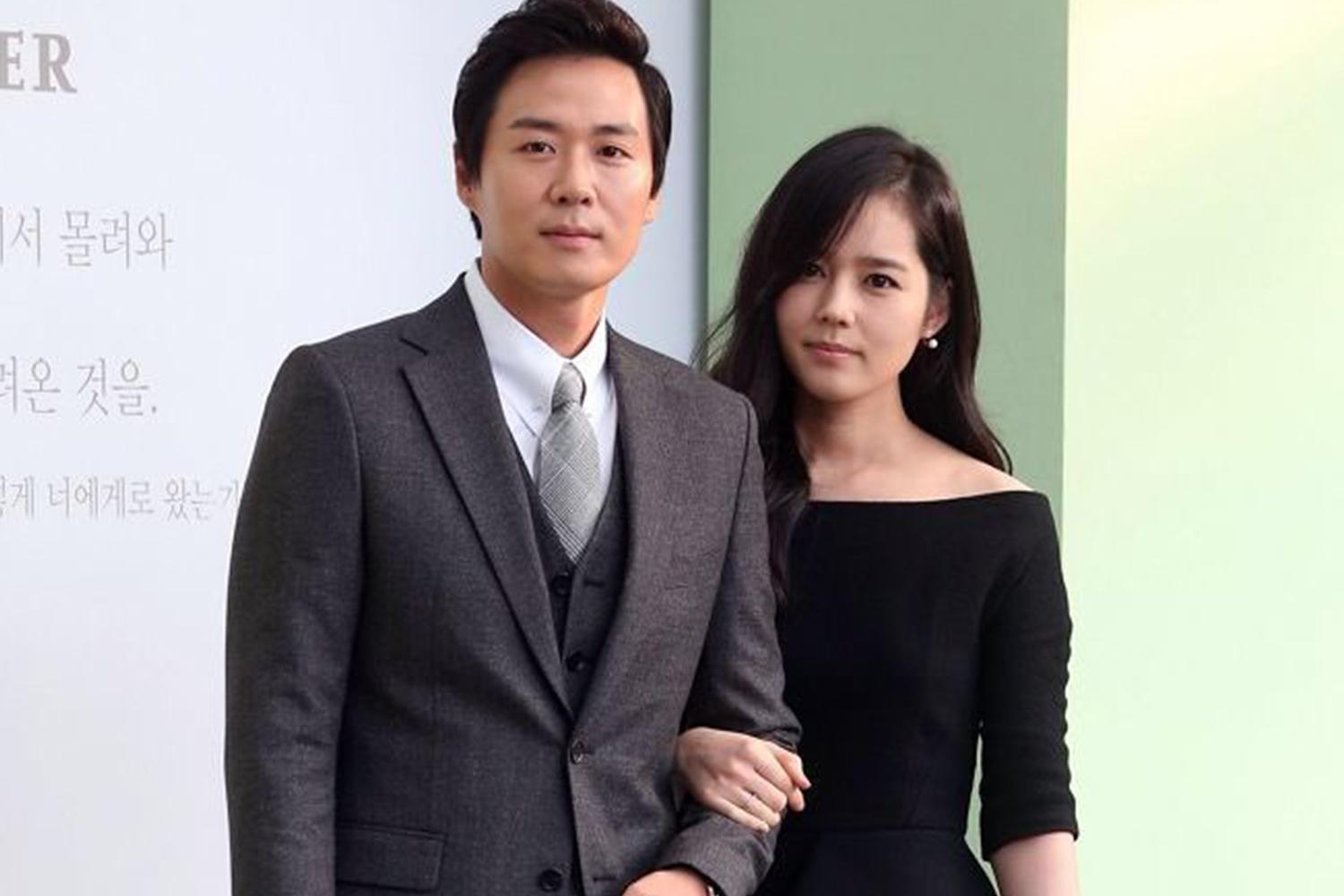 韓國明星情侶合影，男士穿著西裝，女士穿著優雅的黑色連衣裙，兩人親密地環抱在一起。