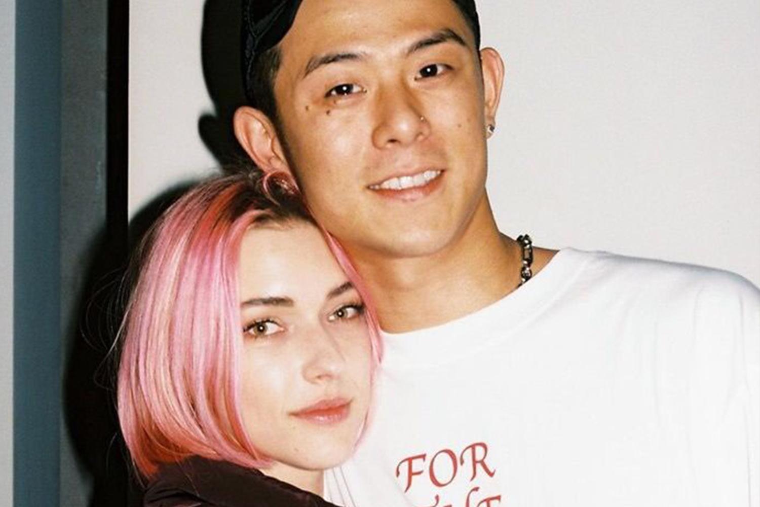 韓國明星情侶，兩人親密地靠在一起，女方染了粉紅色的短髮，男方穿著白色印花T恤，並配戴帽子和項鍊。