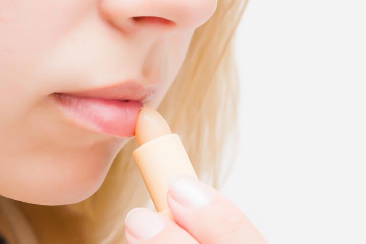 Một người sử dụng tăm bông để bôi son dưỡng lên môi, tượng trưng cho việc chăm sóc môi tỉ mỉ.