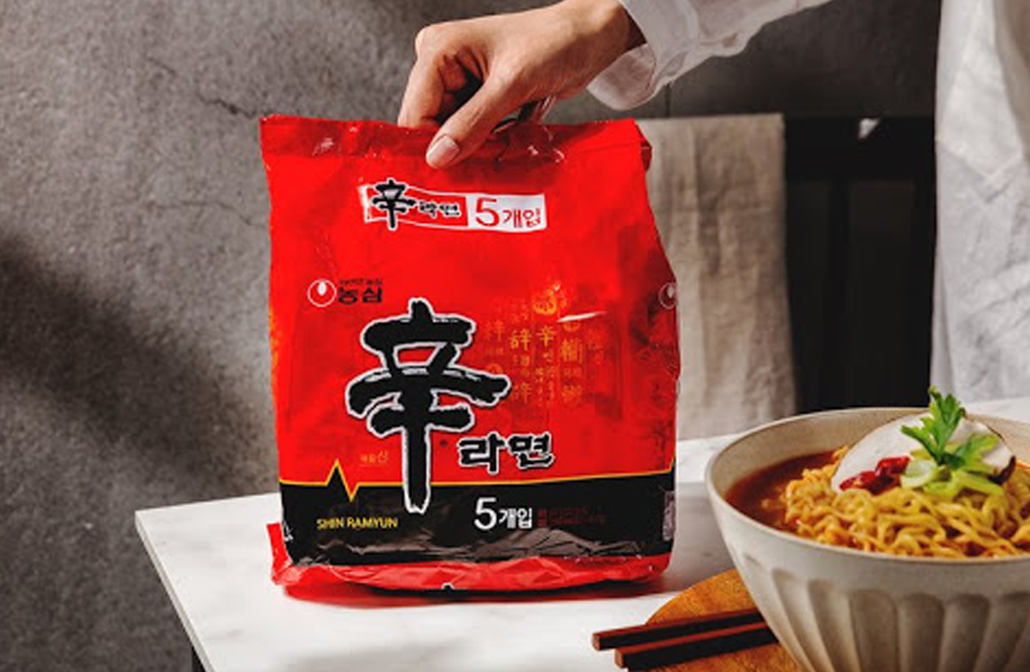 用户手持红色袋装辛拉面，旁边是一碗已煮好的泡面。