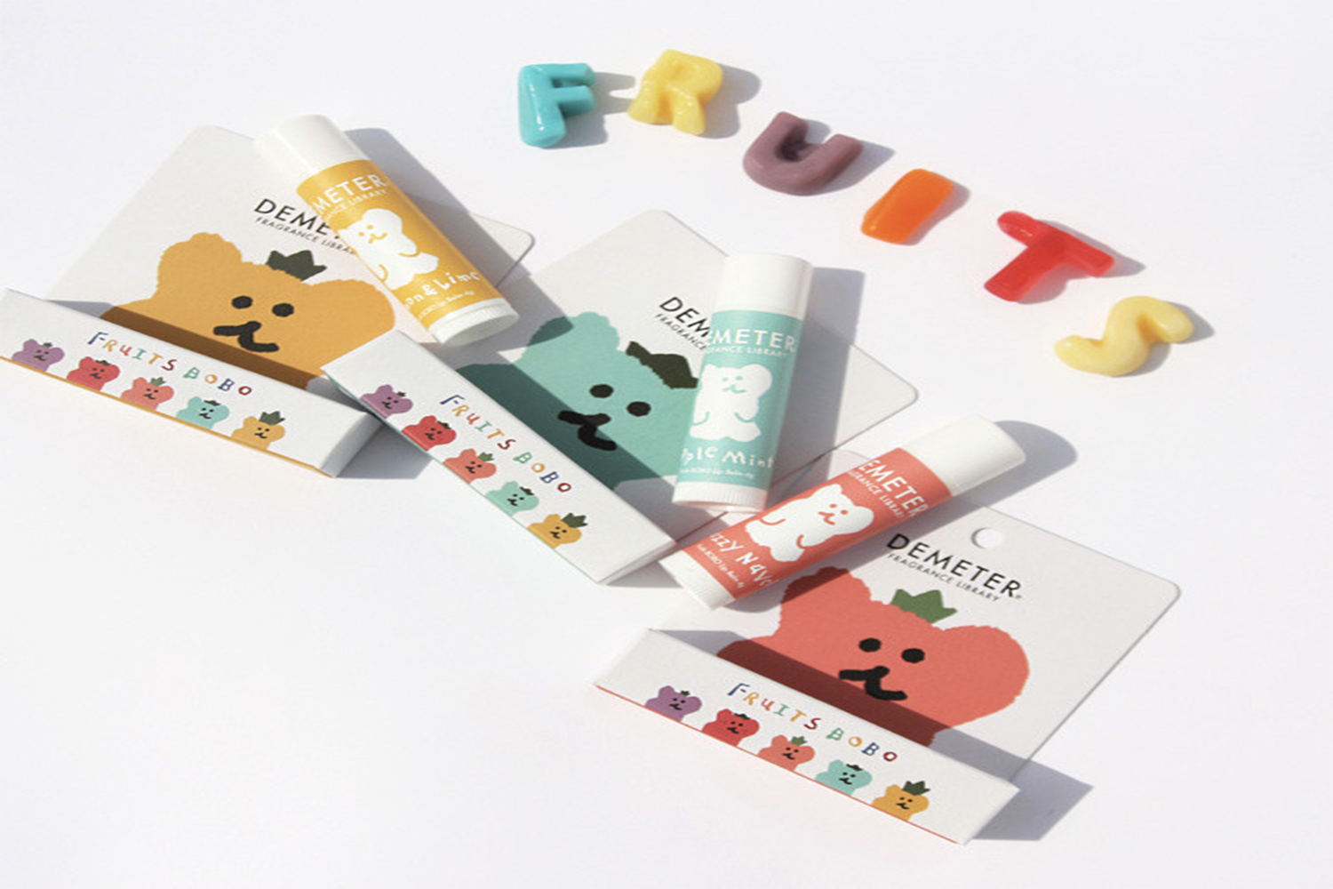香港中環Demeter x Dinotaeng聯名護唇膏展示圖,呈現多種水果香味選擇,背景為白色,有五顏六色的裝飾字母‘FRUITS’。