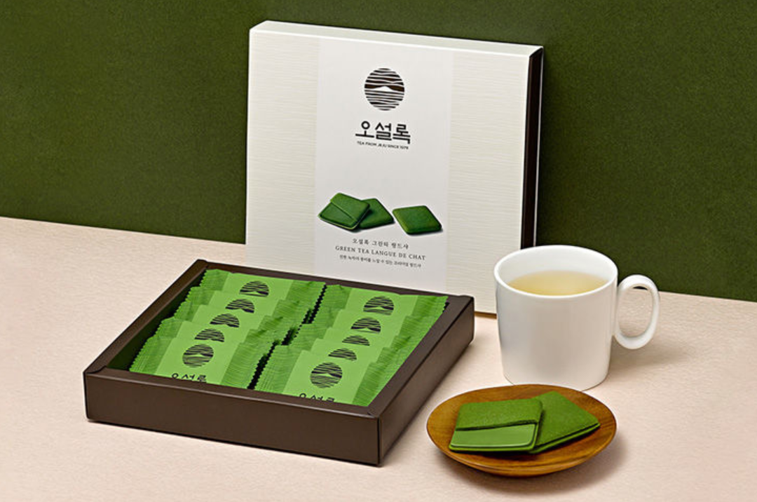 香港中環O'sulloc濟州島綠茶夾心餅乾展示圖,白色的杯子和綠色包裝的餅乾成為搭配,背景為深綠色牆面。