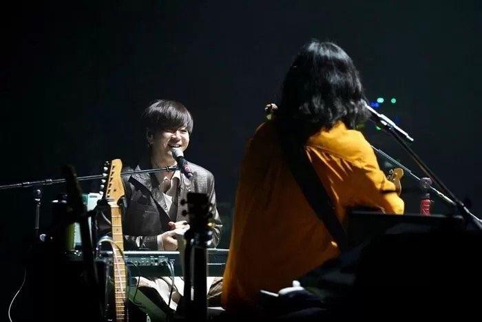 兩位音樂家在演唱會台上演奏儀器，左邊穿著橙色衣服，右邊在鋼琴前坐著