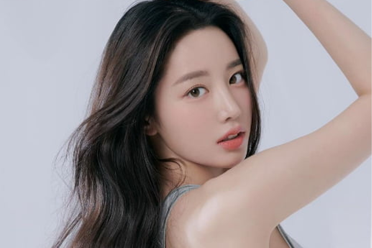 不知名女明星身著鮮艷粉紅色連衣裙,比出韓式心形手勢,呈現青春活潑的風格,背景為白牆。