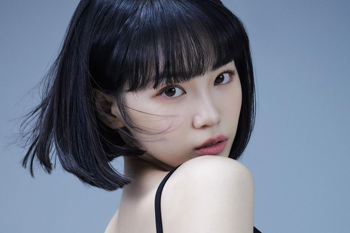 LE SSERAFIM採源身穿黑色露肩洋裝,搭配黑色短髮,背景為藍色。裝飾著紅色花卉,整體給人神秘而沉靜的印象。