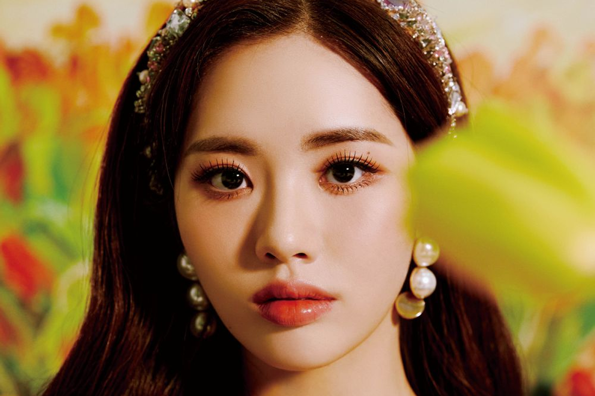 fromis_9成員池原穿著白色露肩禮服,頭戴珍珠耳環,坐在花園背景前,展現優雅的氣質。