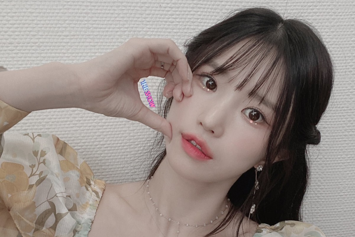 fromis_9成員河英身著花卉圖案連衣裙,手上拿著紙製獎盃,背靠在顆粒牆上,展現清新風格。