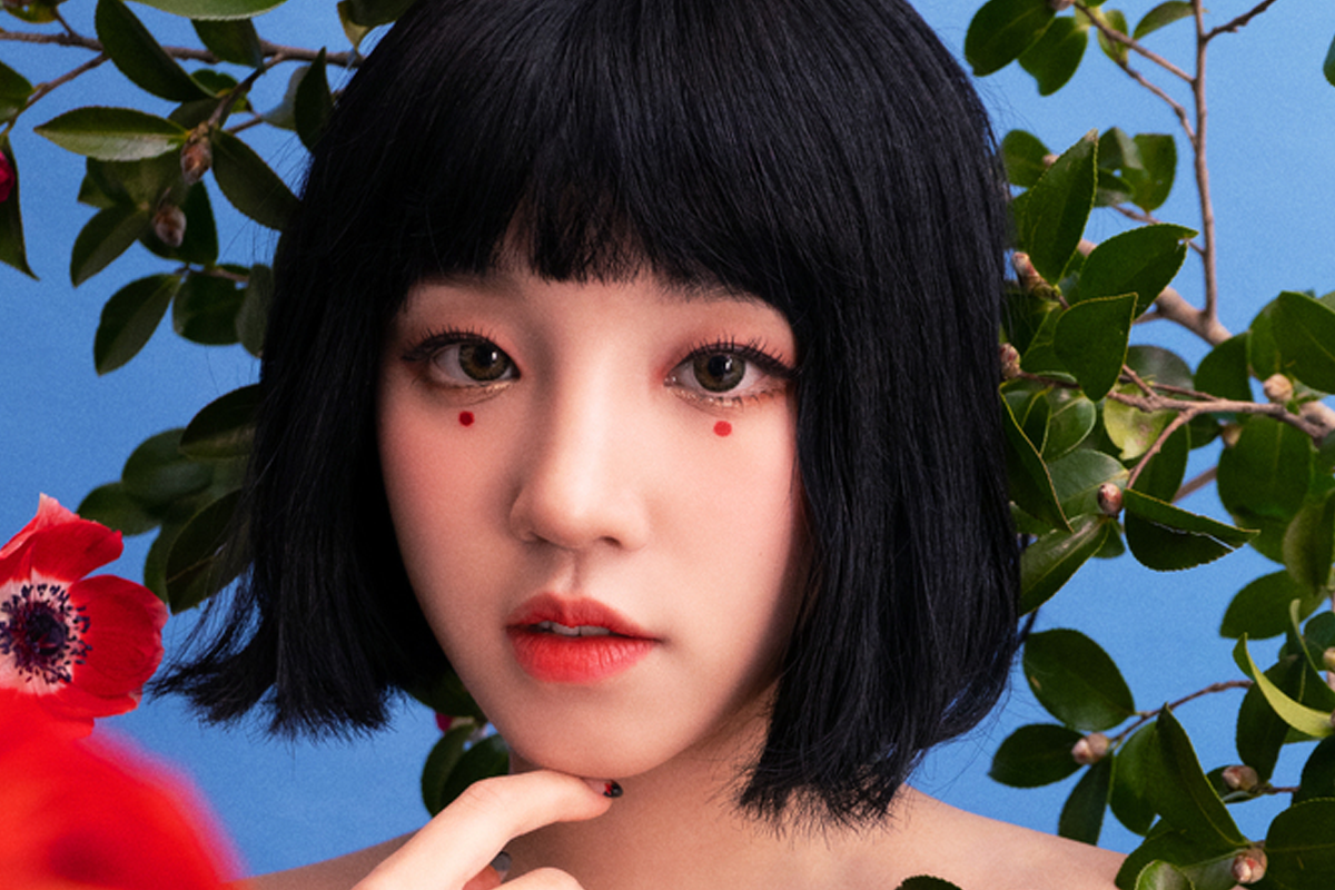 BLACKPINK的Jisoo穿著藍紫色漸變長髮,展示了活潑和可愛的風格,背景是一面粉紅色牆面。