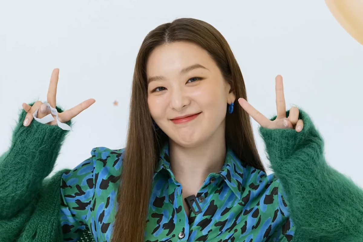 Red Velvet瑟琪穿著藍綠色印花襯衫,並以雙手比出招牌V字手勢,背景為白色,展現青春活力。