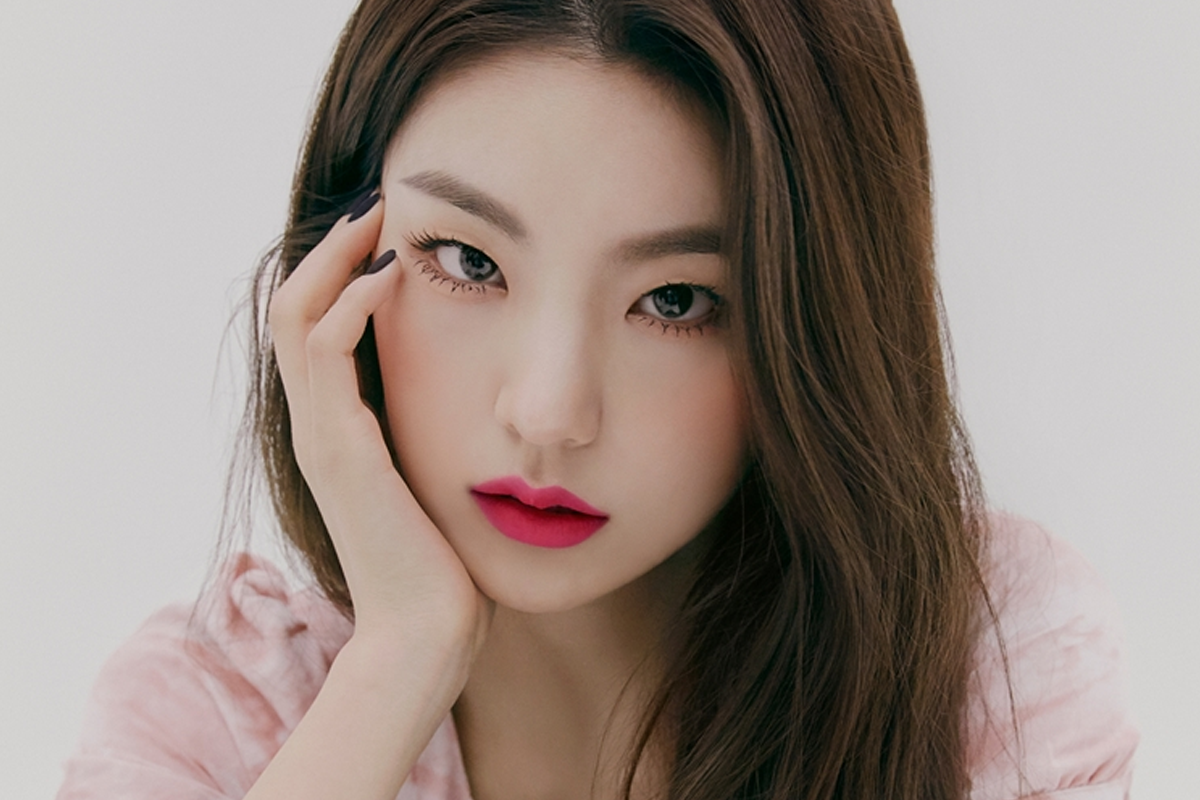 韓國女明星展現出柔和微笑,身穿淺藍色銀色禮服,背景為紫色幕簾,流露出優雅的風範。