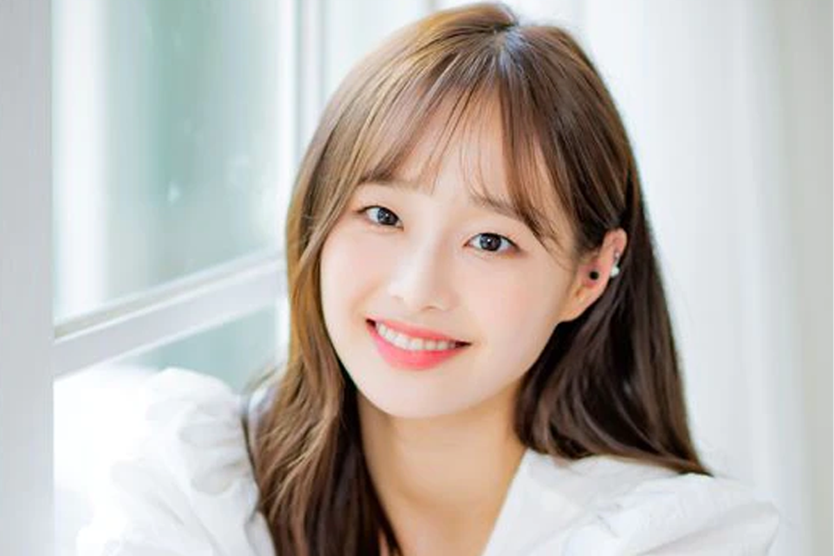 本月少女成員Chuu身著白色襯衫,坐在窗前擺出思考的姿勢,背景為明亮窗外景色,展現知性美。