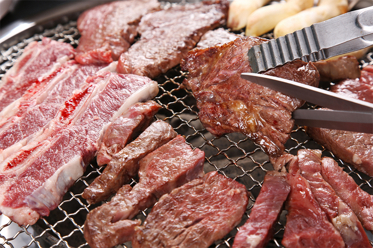 韓國烤肉的場景，肉在燒烤架上被剪刀剪開，以便食用。『剪刀在韓國烤肉料理中的應用』，是一種可體驗韓國美食特色的典型場景。