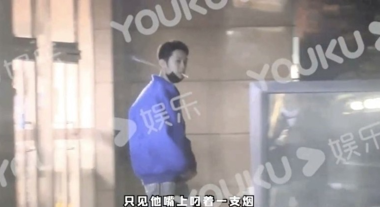 路上で青色のジャケットを着た男性がタバコを持って歩いている場面、背景には中国語の字幕とYoukuの透かしが見える