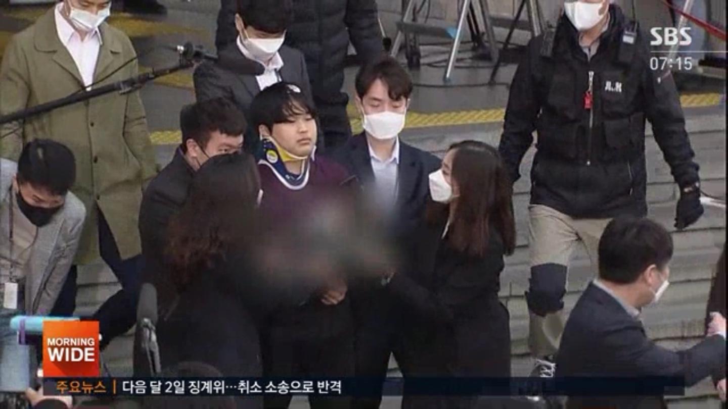 โจกับผู้คุมเดินออกจากอาคาร มีตำรวจและนักข่าวรอบ ๆ คดีนี้เกี่ยวข้องกับการเผยแพร่คลิปอนาจารอย่างผิดกฎหมายในเกาหลีใต้