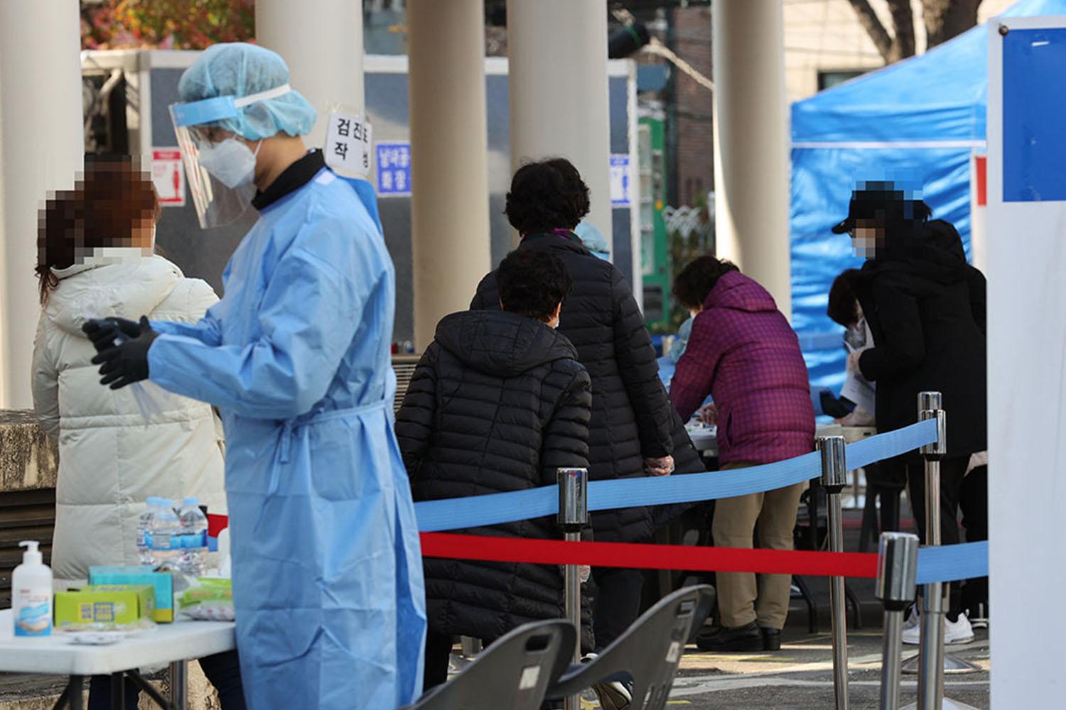 บุคลากรทางการแพทย์สวมอุปกรณ์ป้องกันกำลังดำเนินการตรวจคัดกรองโรคโควิด-19 ให้แก่ผู้คนซึ่งยืนในคิว