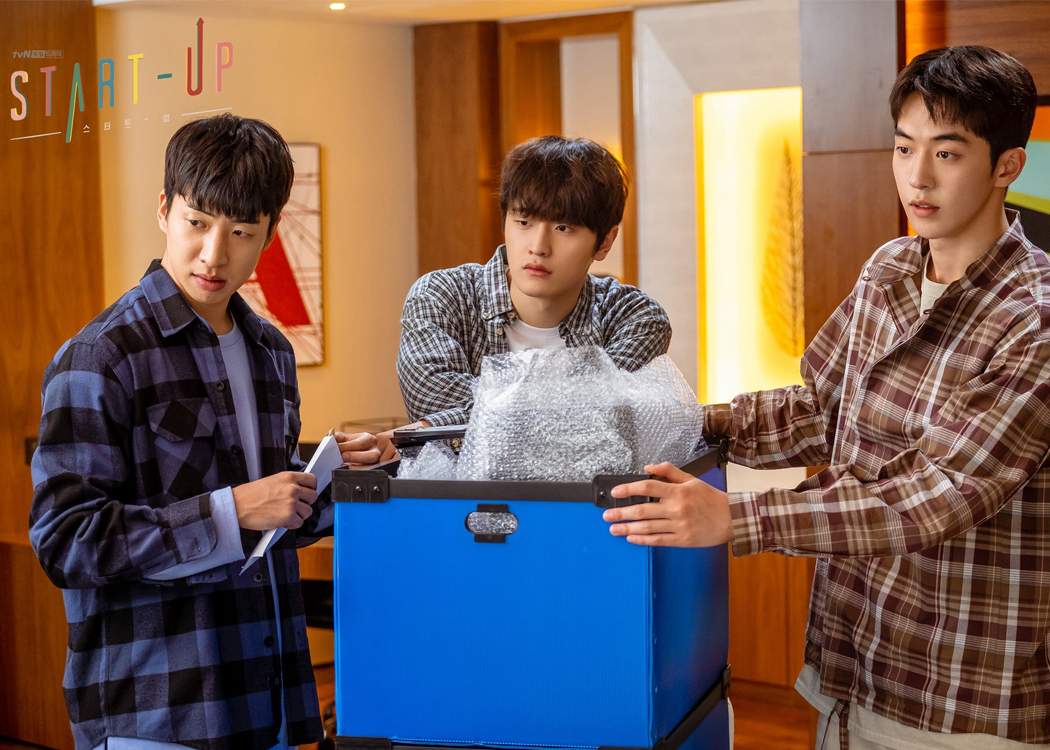 三位角色在公司內部站立，正在處理一個裝滿物品的藍色箱子，充滿創業氛圍。