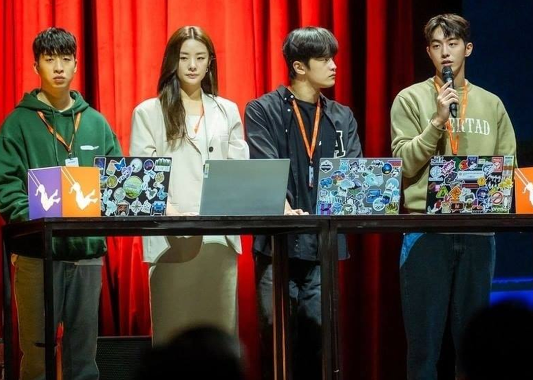 四位青年圍繞著一張桌子，前方放置多臺貼滿貼紙的手提電腦，背景是紅色的幕布。