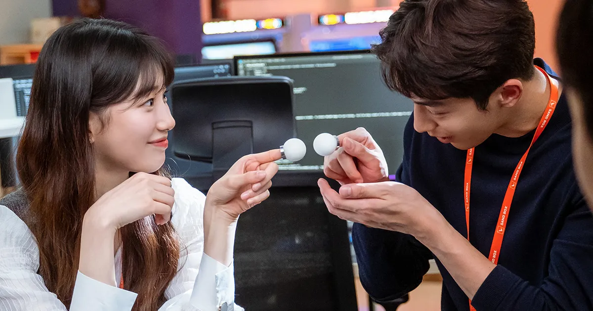 兩位角色在辦公室裡進行小模型的討論與交流，背景是電腦和桌面。