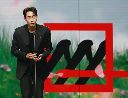 アジアアーティストアワード2020での受賞スピーチに立つ人気俳優。黒いスーツ姿でマイクの前に立ち、会場に語りかけるシーン。