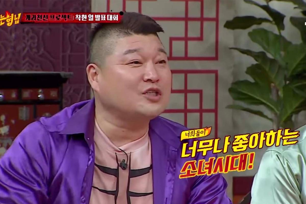 韓國綜藝節目中，姜鎬童穿著紫色上衣，微笑應對主持。」