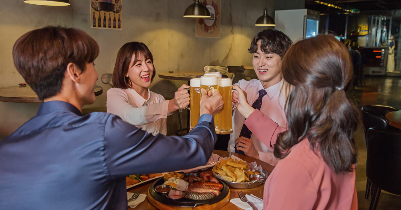 一羣韓國年輕人坐在餐廳的桌子旁喝酒，桌上擺放著各種食物和飲料