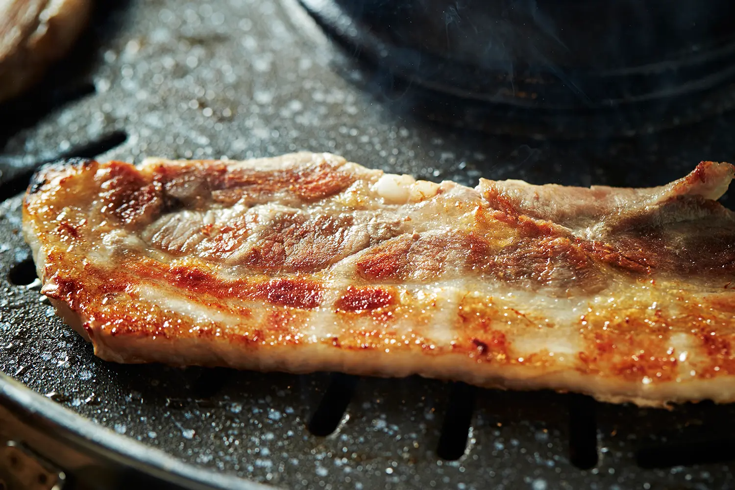 焼いている韓国のサムギョプサル、ジューシーな肉と香ばしい焼き目が特徴的です。三段層の肉で、サンチュと調味料を添えて食べるのが韓国式です。