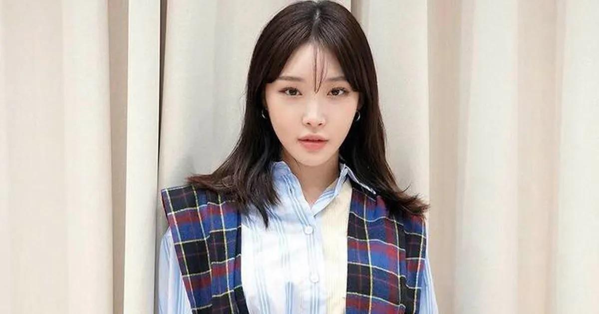 ชองฮาสวมเสื้อเชิ้ตสีขาวพร้อมชุดคลุมลายตาราง กำลังยืนถ่ายรูป ใบหน้าถูกเบลอประกอบข้อมูลข่าวว่าเธอติดโควิด19ในภาพนี้