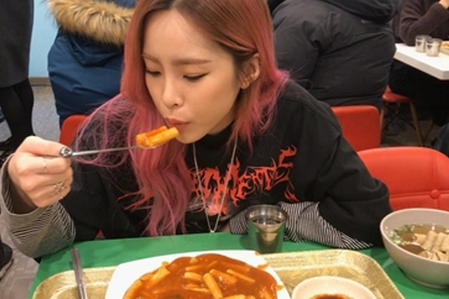 韓國女藝人Heize在快餐店內，右手拿著叉子享用辣炒年糕