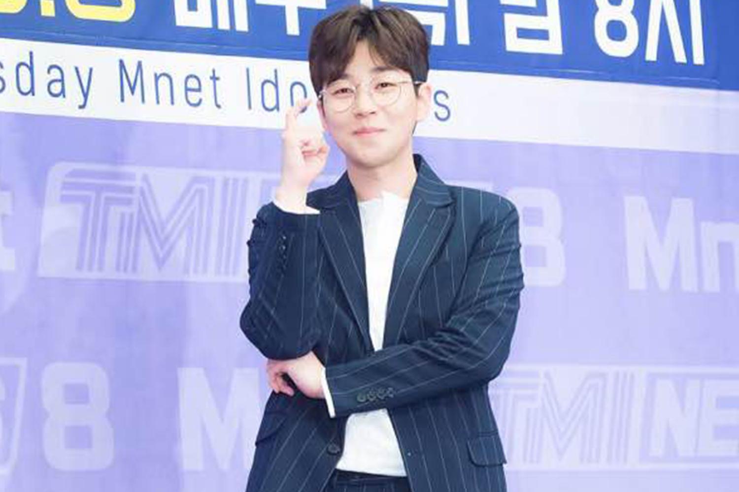 韓國嘻哈歌手DinDin穿著條紋西裝，站在藍色背景前，雙手交叉。