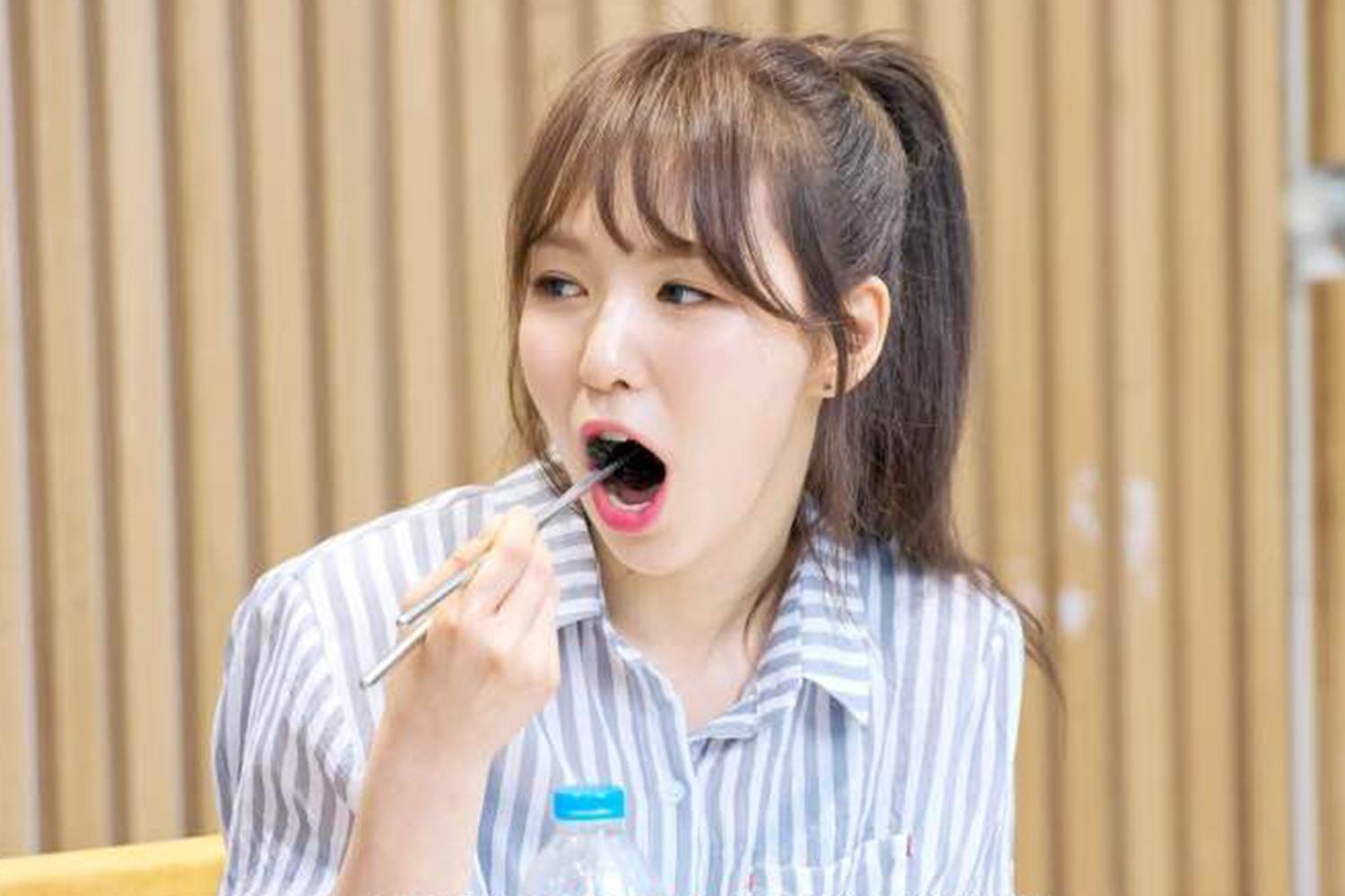 一名韓國女子穿著條紋襯衫，在餐桌前，手持筷子，準備享用餐點。