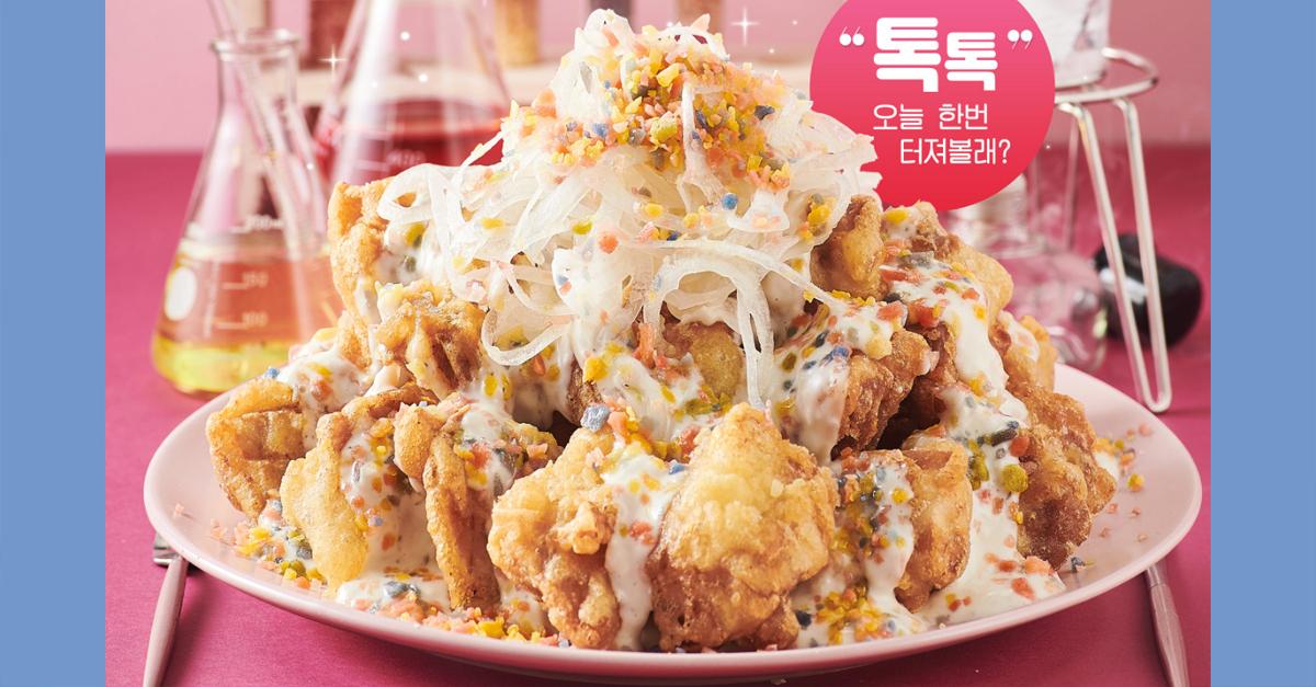 ไก่ทอดเกาหลีโรยด้วยหอมใหญ่และซอสรสน่าชิมในจานสีชมพู บรรยากาศการตกแต่งในสไตล์วิทยาศาสตร์และเครื่องดื่มในแก้วคอแคบ