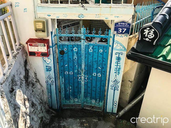 Blue painted gate and wall featuring decorative designs and creative elements in Dongpirang Mural Village.