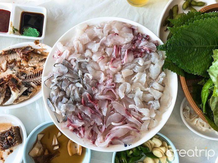 Plate of fresh sliced raw fish served as Korean sashimi with side dishes alongside.