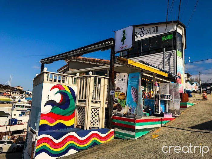 Exterior of a cafe in Dongpirang Mural Village with vibrant wave mural and colorful design.