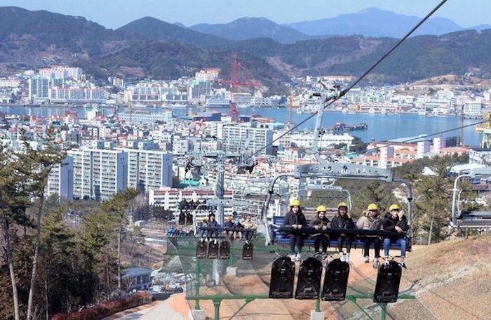 Aerial view of Tongyeong cityscape with several people riding a cable car above.