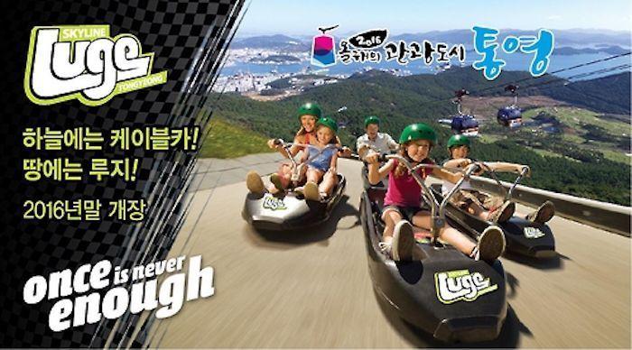 Promotional image for Tongyeong Luge featuring people riding down the hill with city view in the background.