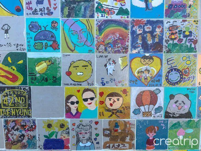 Wall of child-painted tiles featuring colorful art and designs in Dongpirang Mural Village, Tongyeong.