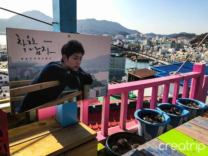 Cafe balcony view overlooking Tongyeong port with poster from a Korean drama series visible.