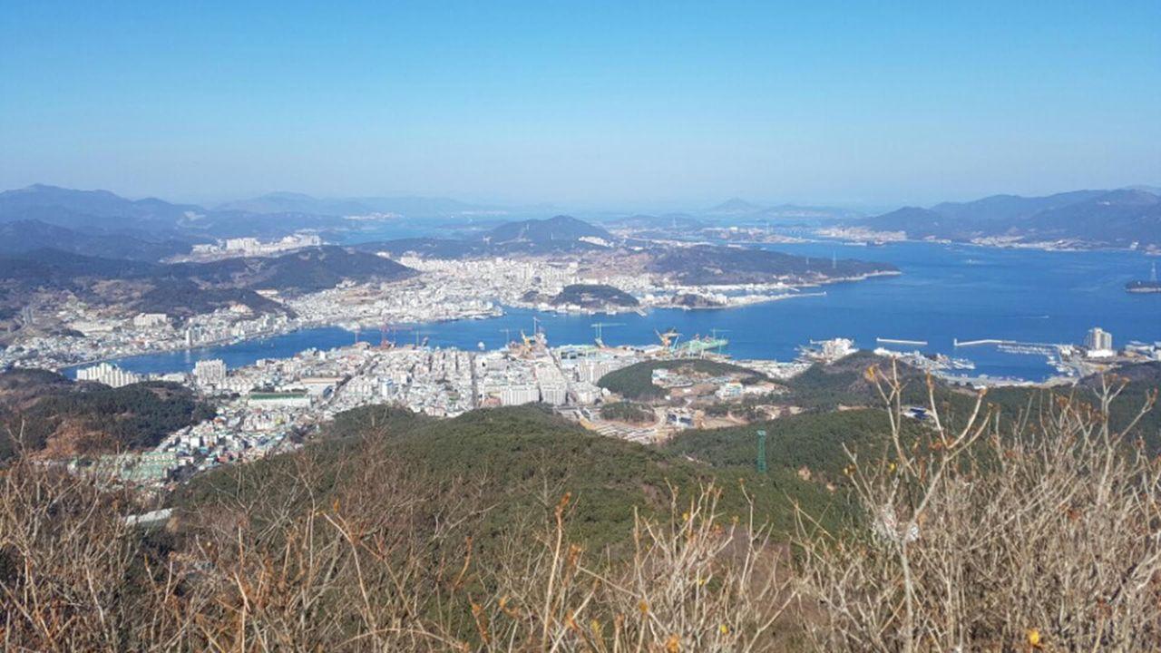 Overlooking view of Tongyeong city with surrounding mountains and sea visible under a clear sky.