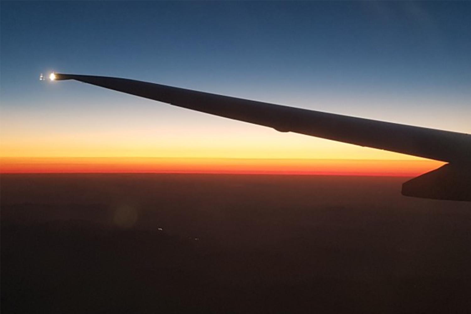 飛機翅膀在空中飛行，背後是美麗的日落景色，展示飛行假期的壯麗空中風景。