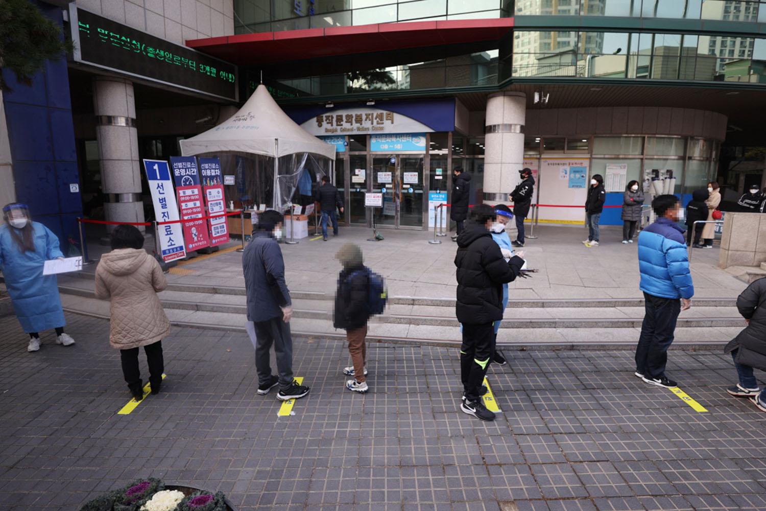 ผู้คนเข้าแถวเพื่อรับการตรวจเชื้อโควิด-19 หน้าศูนย์สุขภาพในเกาหลีใต้ ผู้คนยืนเว้นระยะห่างเพื่อป้องกันการแพร่ระบาด แต่ละคนสวมเสื้อกันหนาวในอากาศหนาวที่บริเวณดังกล่าว