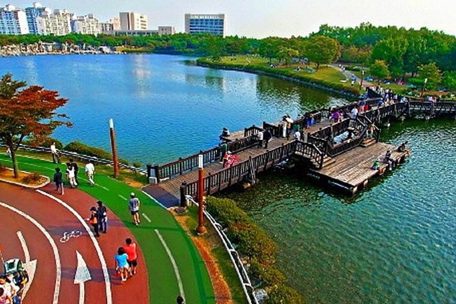 行人在韓國一山湖水公園中享受悠閒時間，背景為湖泊及周邊城市建築