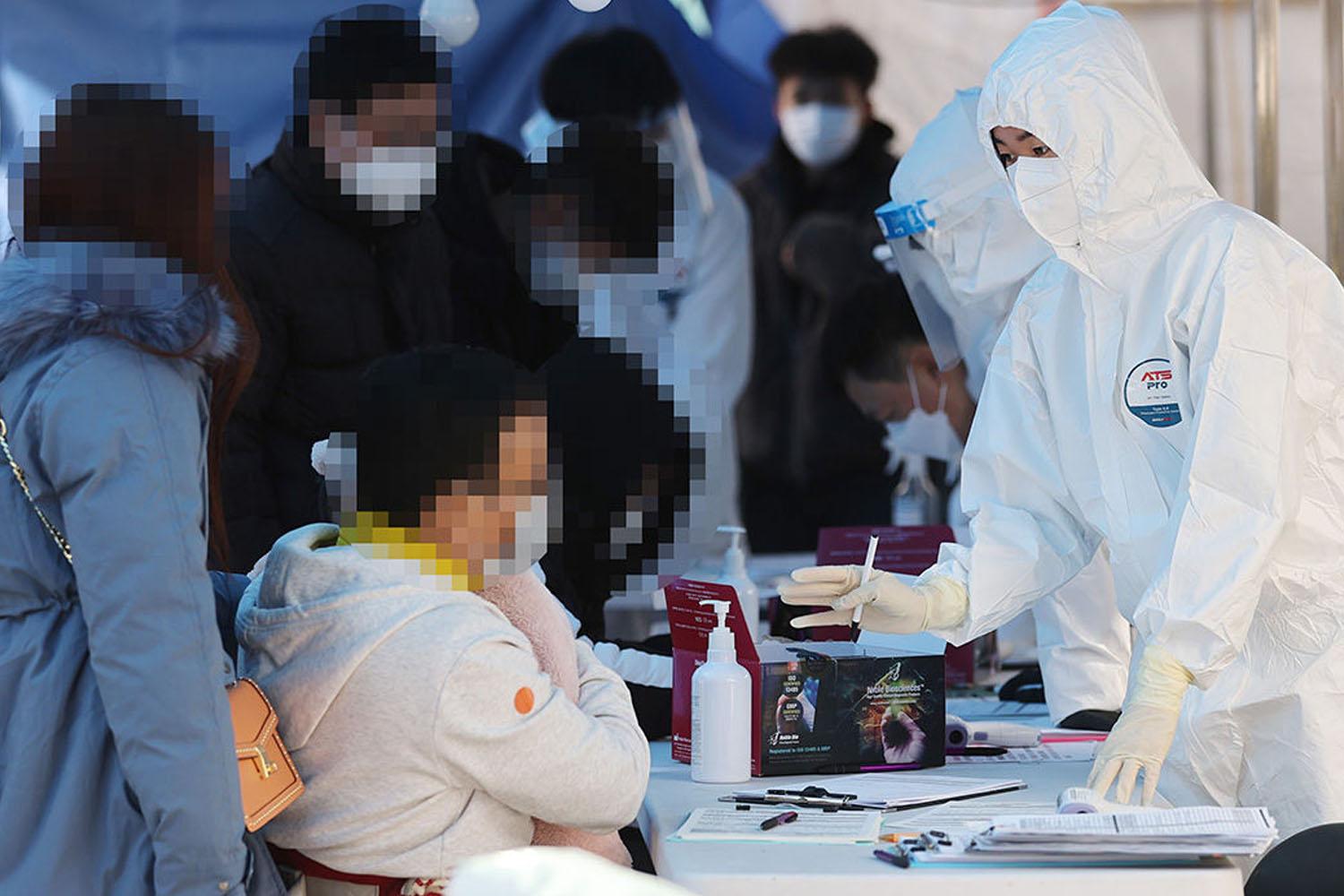 เจ้าหน้าที่ที่แต่งชุด PPE กำลังทำการตรวจโควิด-19 ที่สถานที่ตรวจภาคสนามในเกาหลีใต้ ขณะที่มีประชาชนจำนวนมากเข้ามารับการตรวจสอบและรอคอยอย่างมีระเบียบ