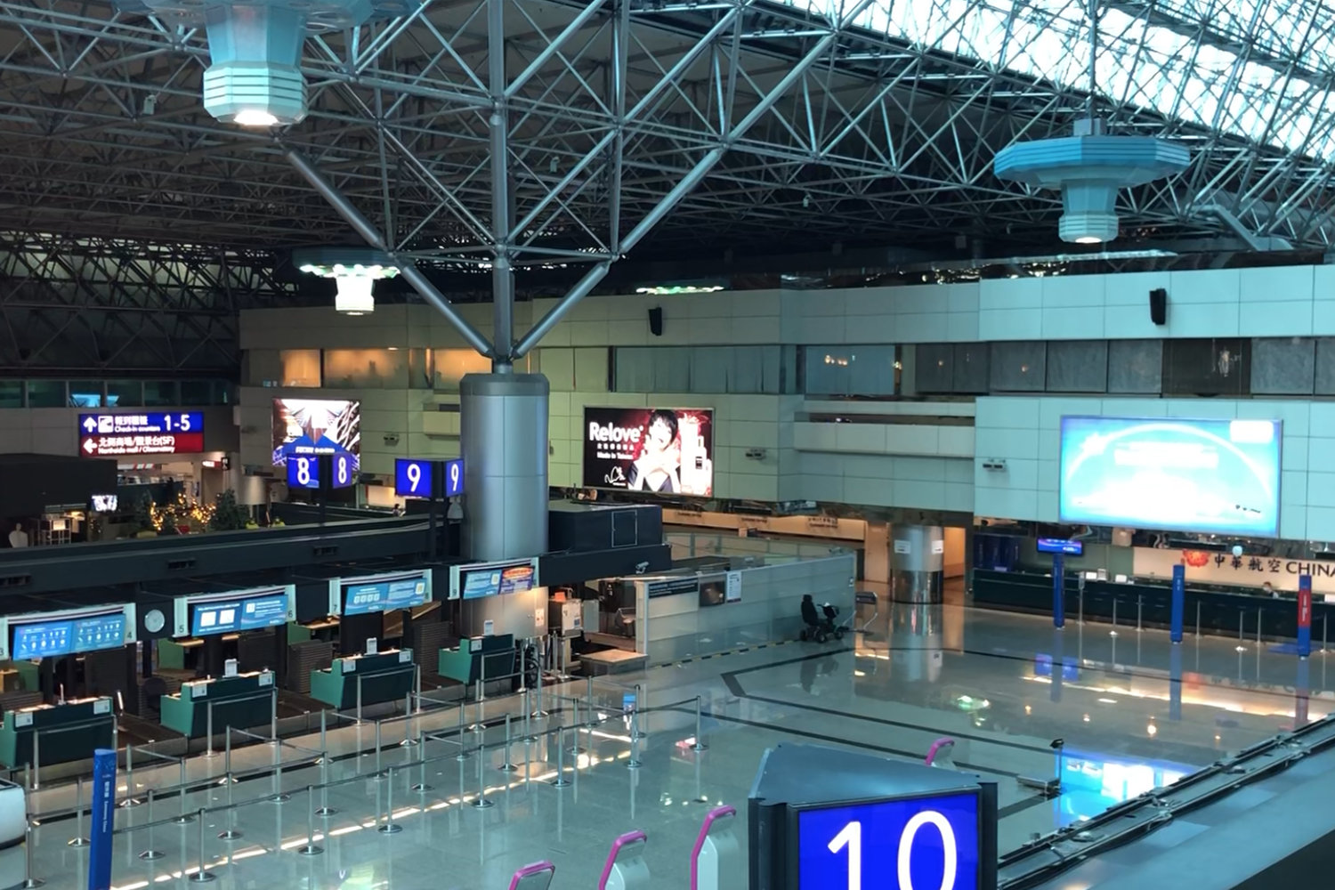 Vista interior de un aeropuerto vacío con mostradores de registro sin actividad y señalización iluminada.