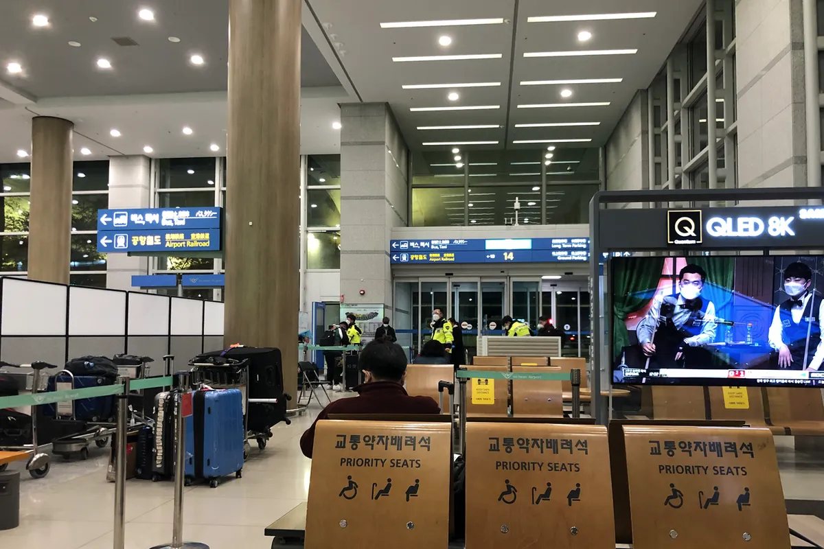 Interior del aeropuerto de Incheon con señalización de asientos prioritarios y personal de seguridad llevando mascarillas.