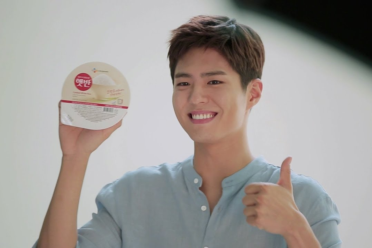 即食米飯廣告，模特穿著淺色襯衫，左手拿起產品右手比出大拇指。