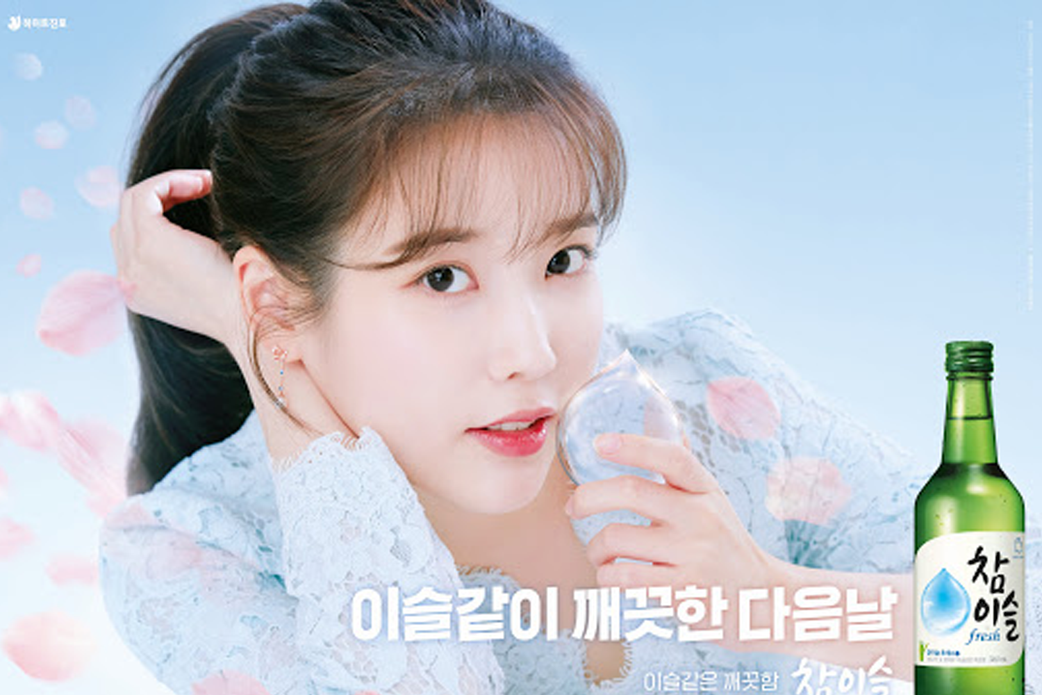 韓國燒酒飲品圖像廣告，背景是藍天和櫻花花瓣，模特拿著標有韓文字樣的酒瓶。