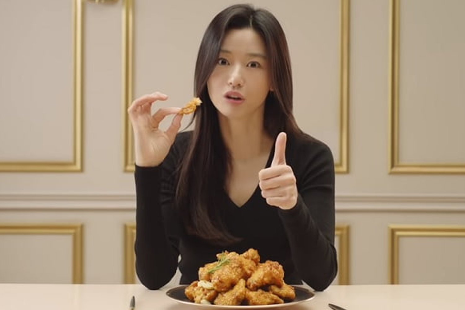 炸雞廣告，模特坐在豪華背景中，桌上放著一盤炸雞並豎起大拇指。